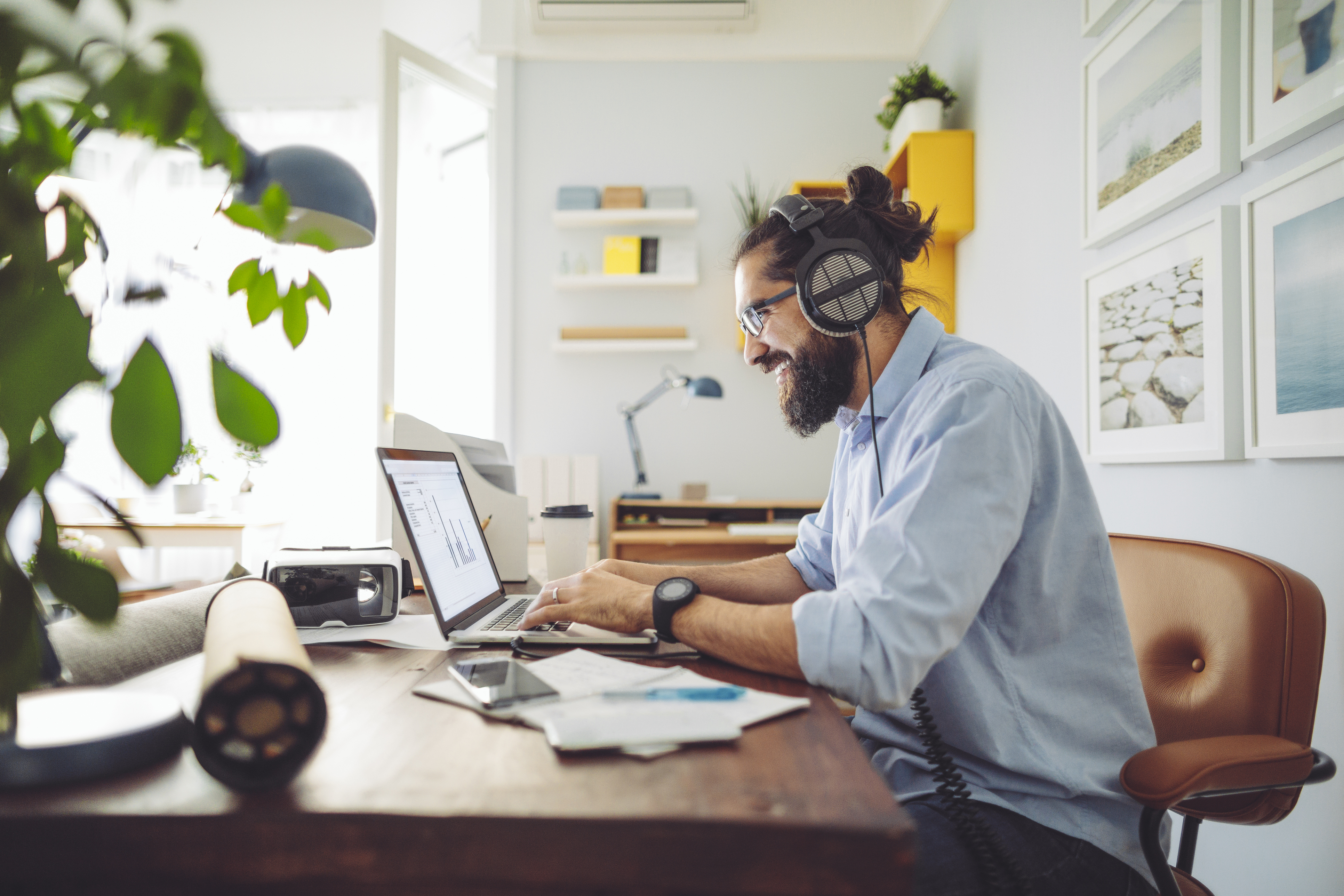 Man at desk with headphones on uses a laptop