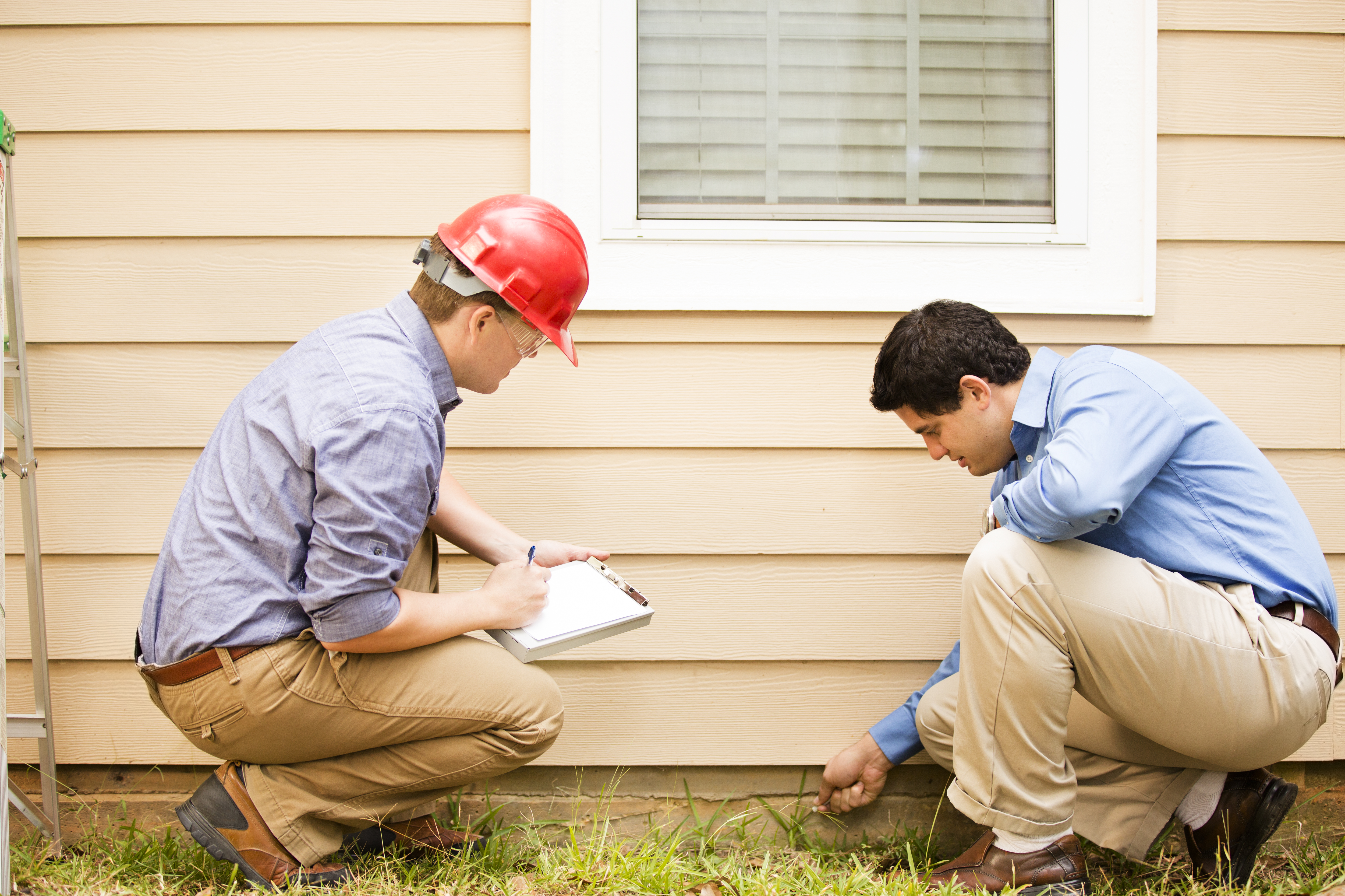 Two inspectors examining the side wall of a house
