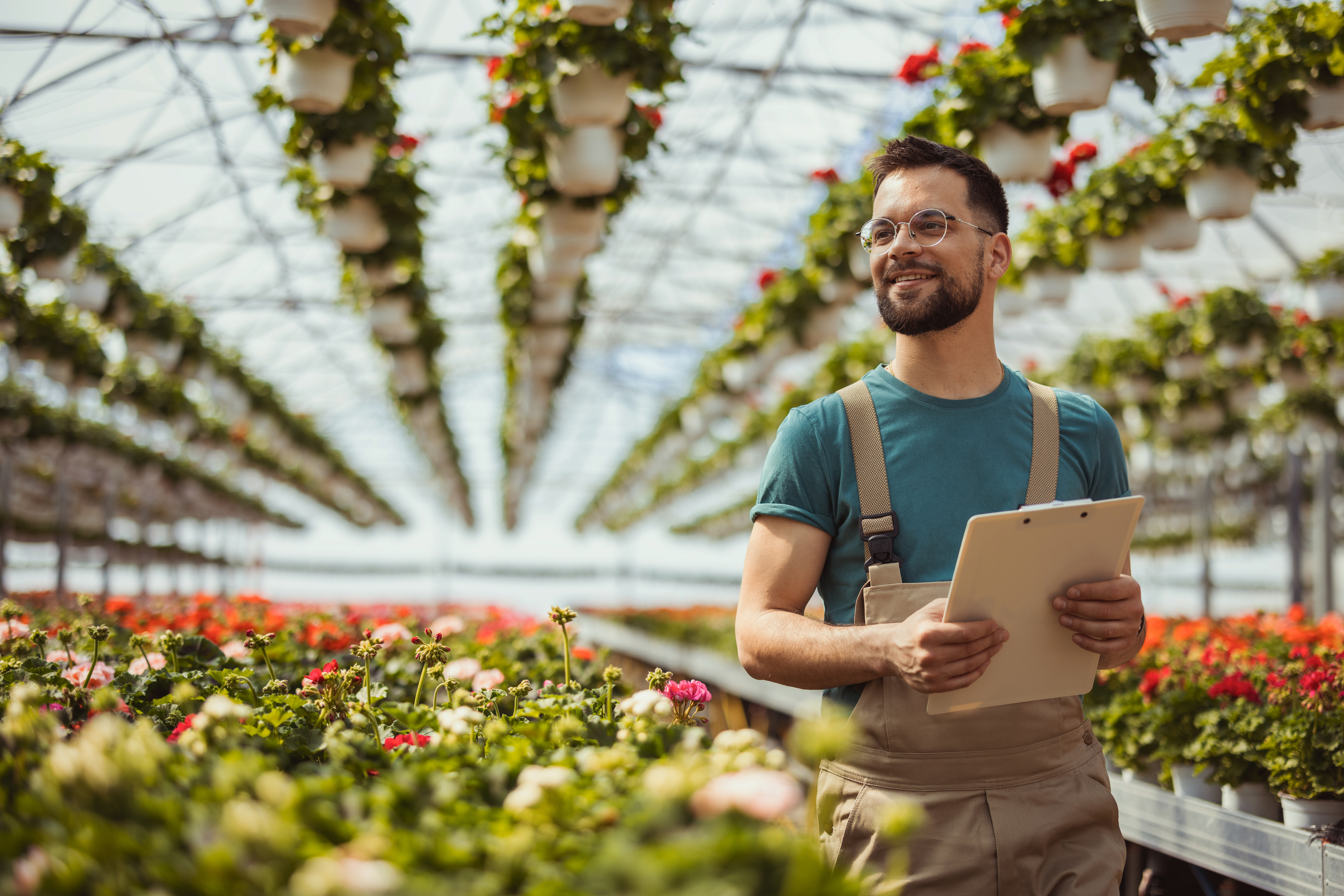 Greenhouse worker stands in front of plants while holding a clipboard.