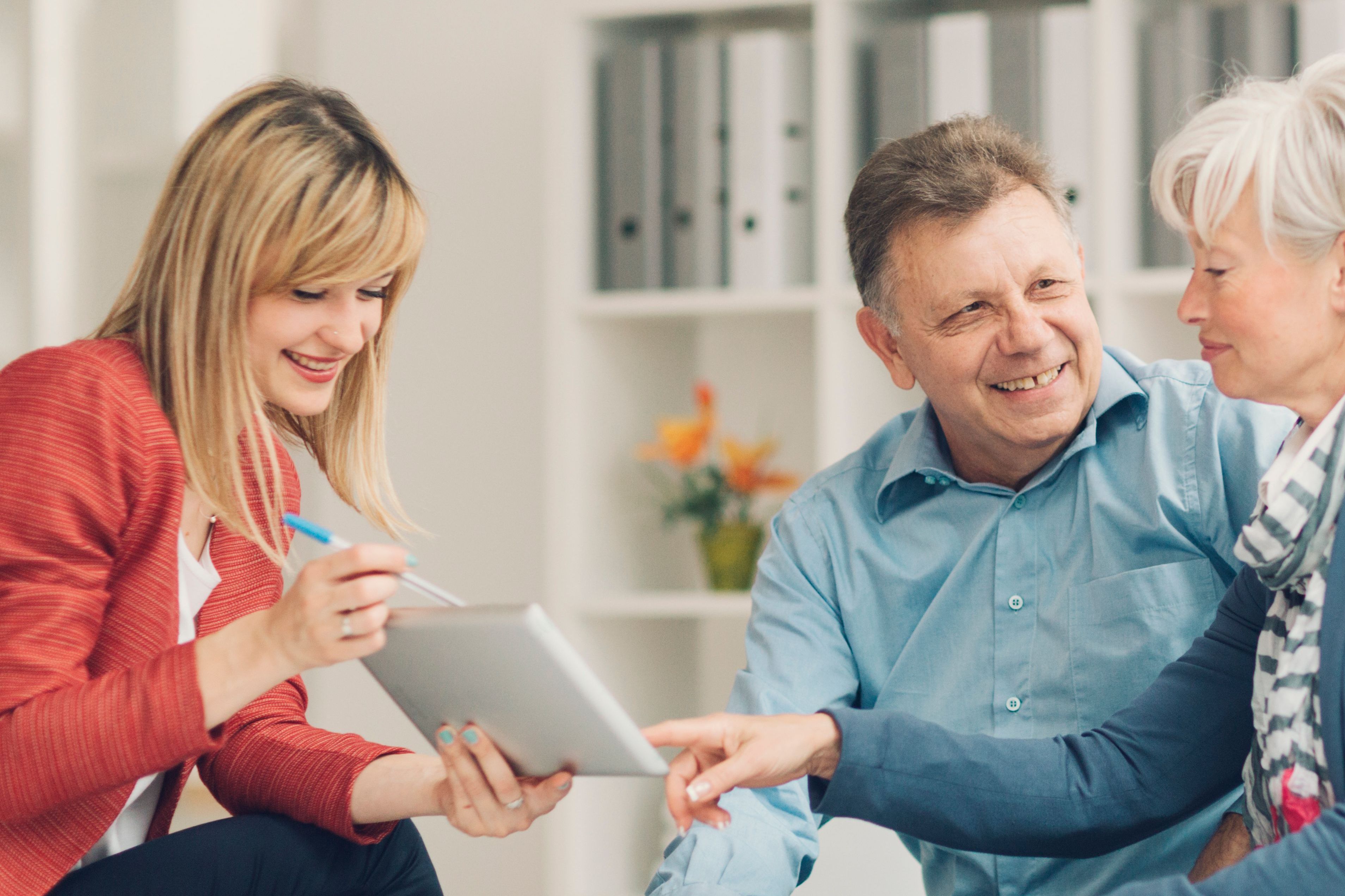 Mature Woman pointing with index finger to digital tablet and asking financial advisor for explanation.